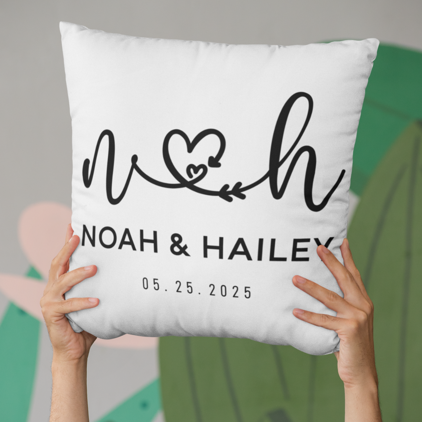 White pillow with personalized name and date design held by hands against a blurred background