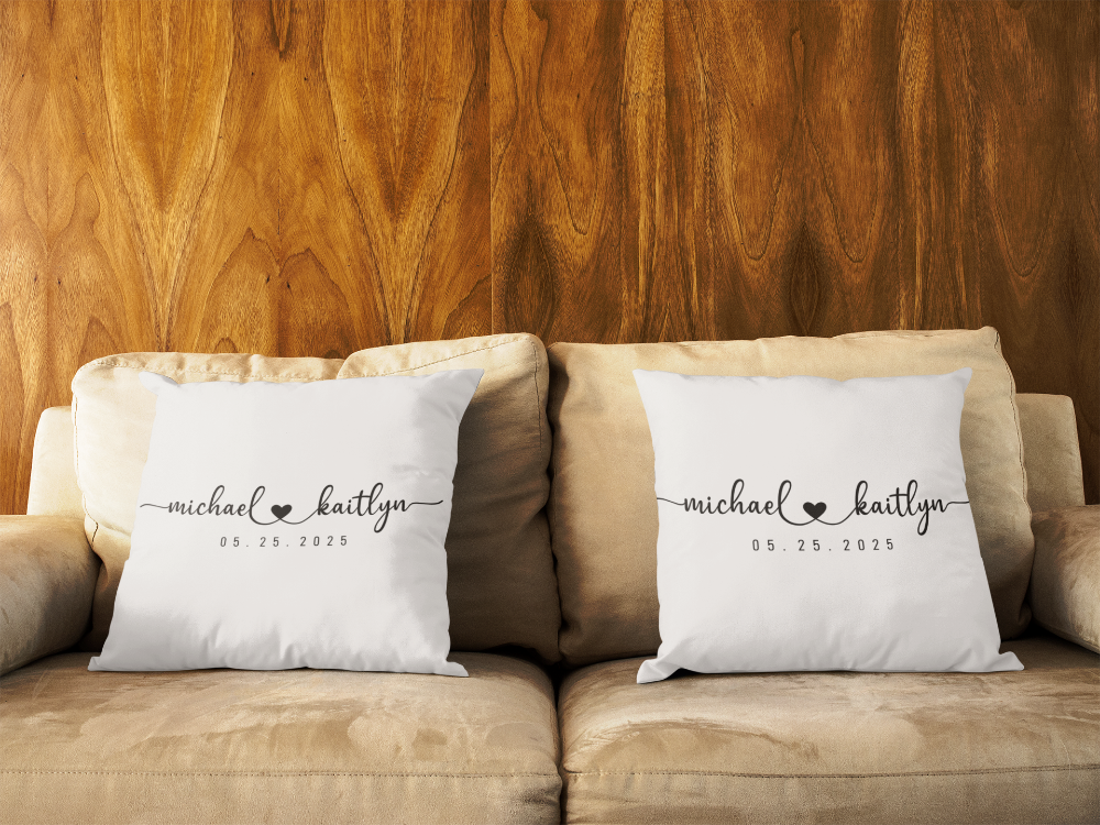 Two white pillows with personalized names on a beige couch against a wooden wall.