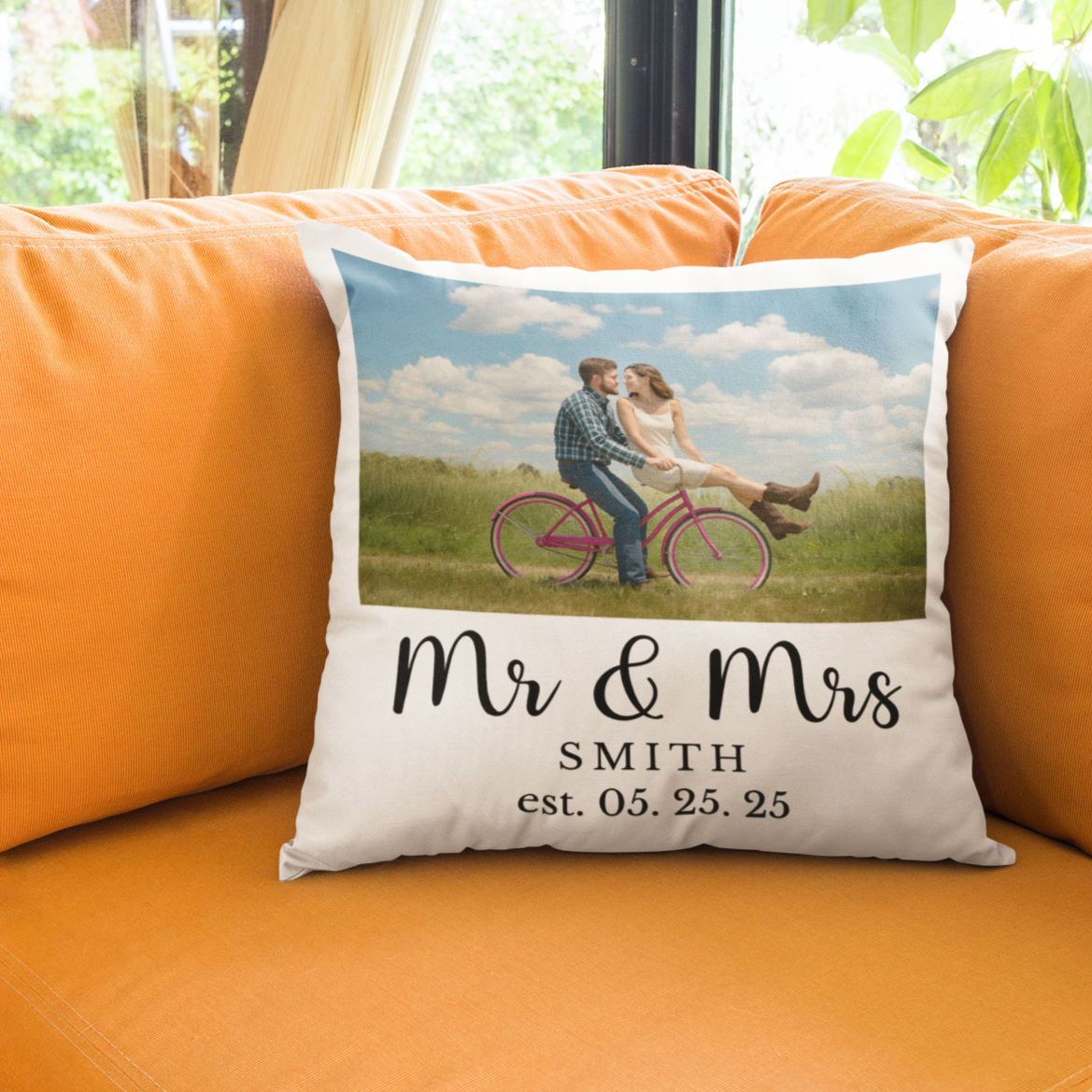 Decorative pillow with a couple on a bicycle and 'Mr & Mrs Smith' text on an orange couch.
