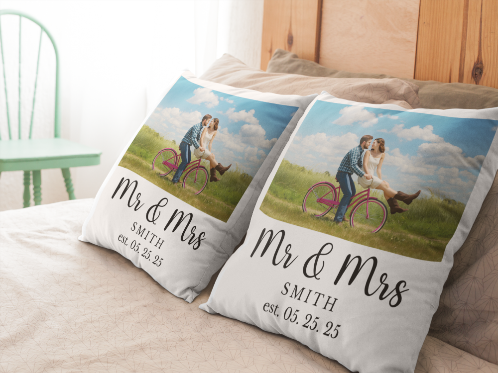 Two decorative pillows with a couple on a bicycle and personalized text on a bed.