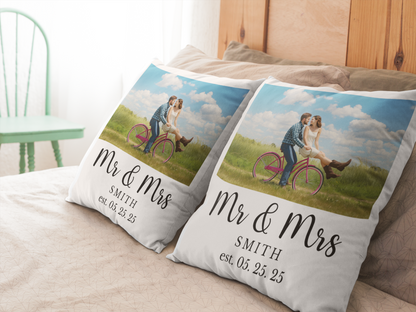 Two decorative pillows with a couple on a bicycle and personalized text on a bed.