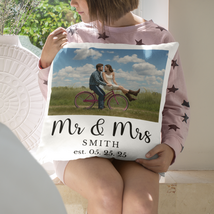 Person holding a pillow with a printed design and text in a room with a window and plant.