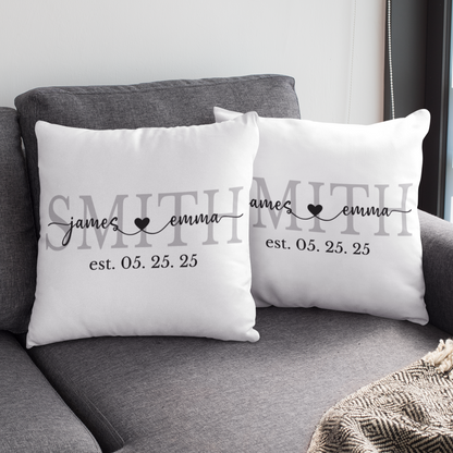 Two white pillows with personalized text on a gray couch with a coffee cup on a small table.